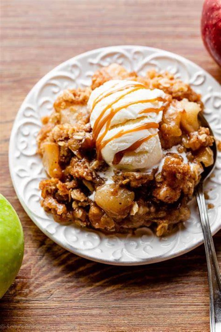 Apple crisp on a white plate topped with vanilla ice cream and caramel sauce.