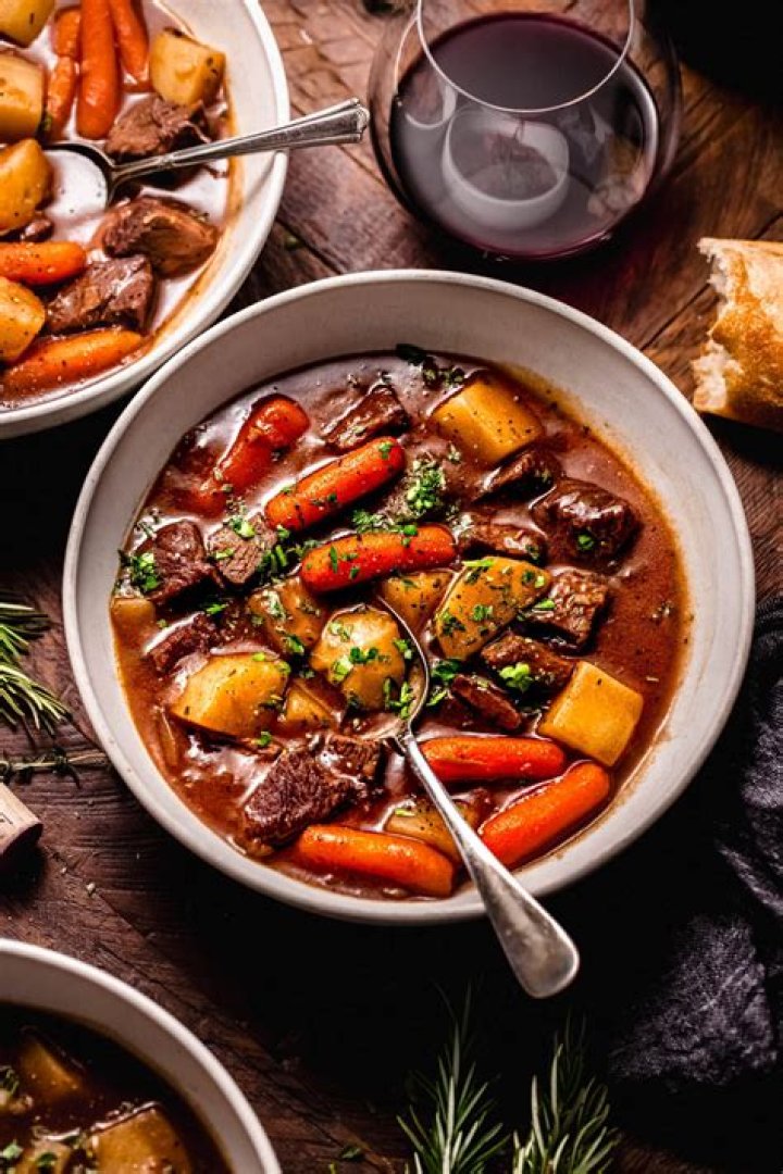 Beef stew and red wine with a loaf of bread in the background.