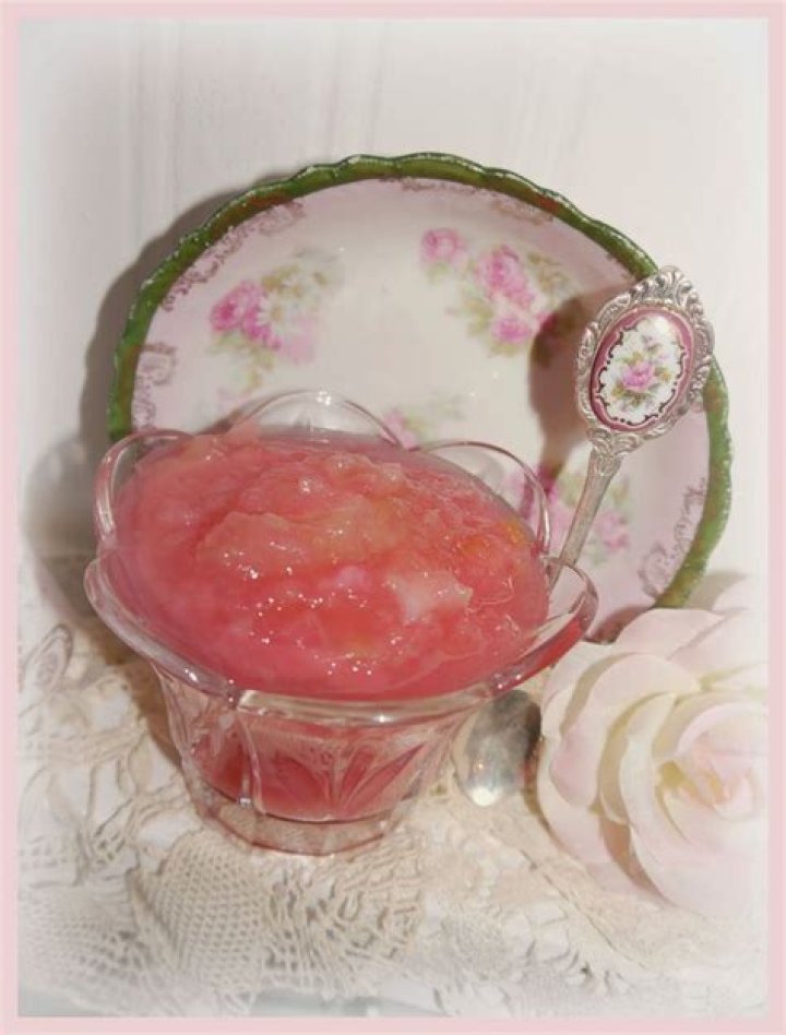 Pink applesauce in a glass jar with a wooden spoon.