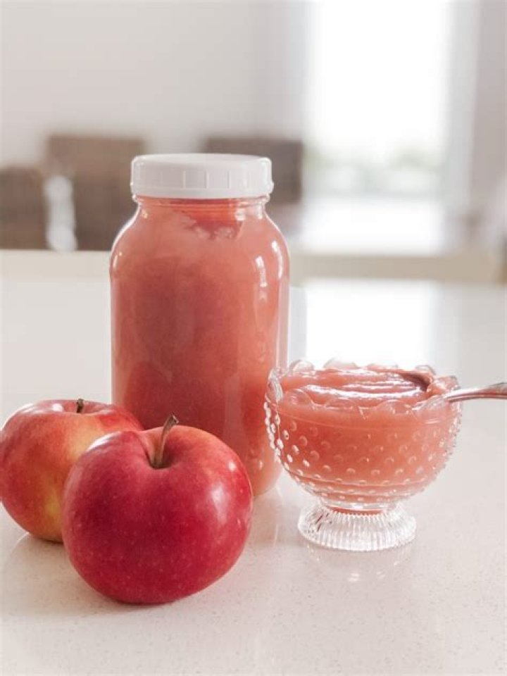 Pink applesauce in a white bowl with a cinnamon stick.