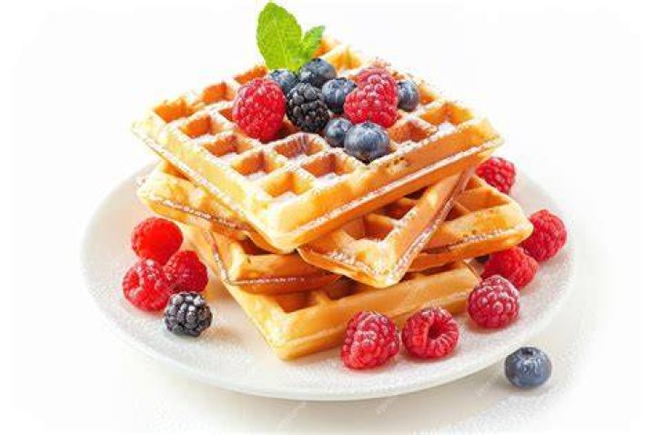 White plate with waffles, berries, and whipped cream.
